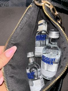 a hand holding a purse filled with bottles of vodka and another bottle in the back pocket