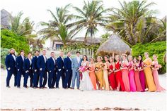 a group of people standing next to each other on top of a sandy beach in front of palm trees