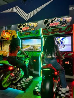 two people playing video games on motorcycles in a room with neon lights and checkered flooring