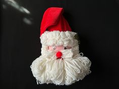 a white santa clause with a red hat on it's head is hanging from a black wall