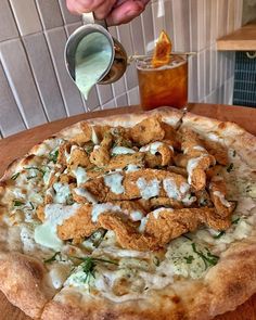 a person pouring sauce onto a pizza on a wooden table with other food and drinks