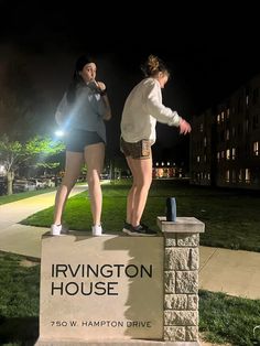 two girls standing on top of a sign in front of a building at night time