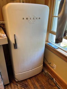 an old white refrigerator sitting in the corner of a room next to a window with no curtains