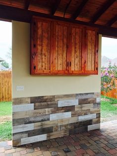 an outdoor fireplace with wooden shutters on the side and brick pavers around it