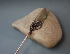 a feather quill sitting on top of a rock next to a metal hook with a bead in it