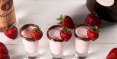 four glasses filled with milk and strawberries next to a bottle