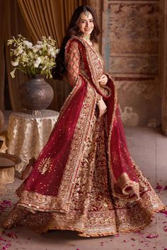 a woman in a red and gold bridal gown standing next to a vase with flowers