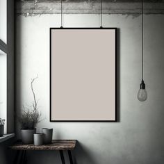 an empty poster hanging on the wall next to a table with two planters and a light bulb