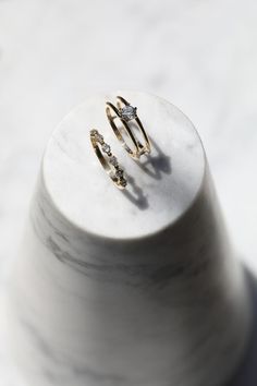 two gold rings sitting on top of a white marble stand with one diamond in the middle