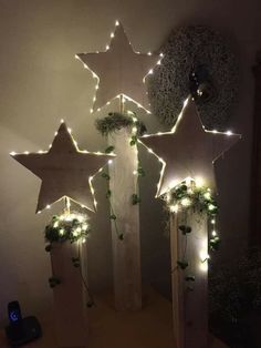 five wooden stars are decorated with greenery and lite up by fairy lights on the wall