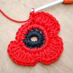 a crocheted red flower with black center sits on a table next to a pair of scissors