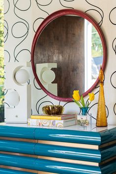 a blue dresser topped with books and a round mirror