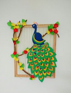 a paper peacock sitting on top of a tree branch next to a wooden framed frame