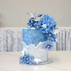 a blue and white frosted cake with flowers on the top is sitting on a table