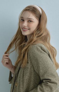 a young woman with long hair wearing a headband smiling at the camera while standing against a blue wall