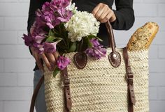 a woman holding a woven bag with flowers in it and a loaf of bread on the side