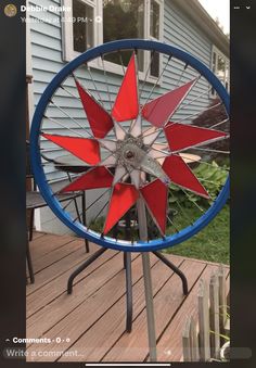 a red, white and blue spinning wheel sitting on top of a wooden deck next to a house