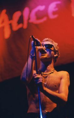 a shirtless man holding a microphone in front of a red and white sign that reads alice