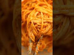 a close up of spaghetti being held by two tongs in front of the camera