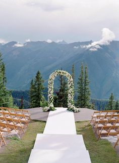 an outdoor ceremony setup with white flowers and greenery on the aisle, surrounded by mountains