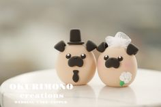 two wedding cake toppers made to look like pugs with hats and flowers on their heads