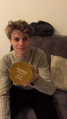 a man sitting on top of a couch holding up a gold plaque that says i'm cold