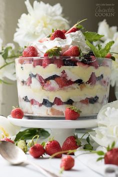 a trifle with strawberries and whipped cream on top is sitting on a cake stand