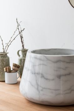 a white marble bowl sitting on top of a wooden table next to two vases