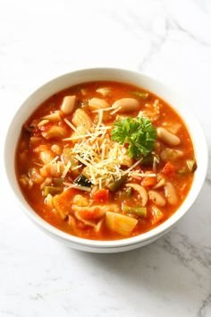 a white bowl filled with lots of food on top of a marble counter next to a wooden spoon