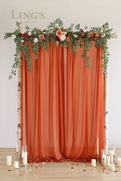 an orange backdrop with flowers and greenery on it is surrounded by candles in front of the curtain