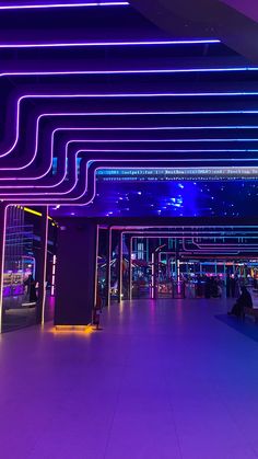 an empty room with purple lighting and people sitting on benches in the background at night