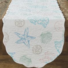 a table runner with shells and starfishs on it, sitting on a wooden surface