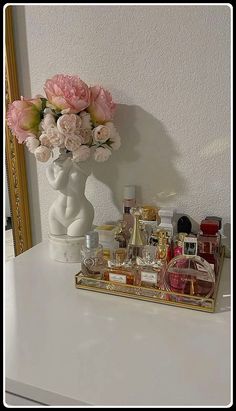 a white vase filled with pink flowers on top of a table next to a mirror