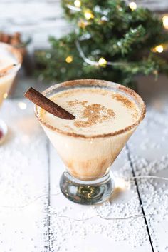 two glasses filled with drinks sitting on top of a table next to a christmas tree