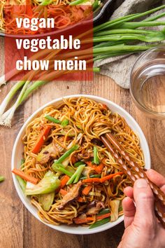 a bowl of vegetable chow mein with chopsticks in it on a wooden table