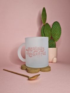 a white coffee mug sitting on top of a table next to a cactus