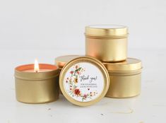 three gold tins filled with candles sitting on top of a white table next to each other