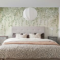 a large bed sitting under a white light next to a wall with leaves on it