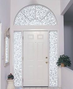 a white front door with an arched window and potted plant on the floor next to it