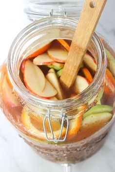 a jar filled with sliced apples and oranges next to a wooden spoon on top of a marble counter