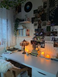 a white desk topped with lots of candles next to a wall covered in pictures and photos