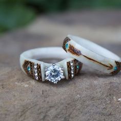 two wedding rings sitting on top of a rock with a diamond in the center and turquoise stones around them