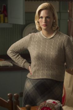 a woman standing in front of a table wearing a sweater and skirt with her hands on her hips