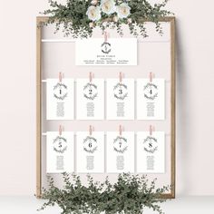 a wedding seating chart with white flowers and greenery on the wall next to it