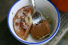 a bowl filled with cake and frosting on top of a wooden table next to an orange pumpkin