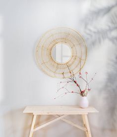 a white vase sitting on top of a wooden table next to a round wall mirror