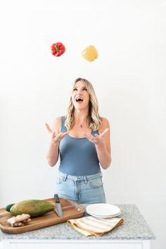 a woman standing in front of a counter with food flying above her and making an odd face