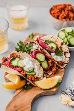 three tacos with cucumbers, onions and sauce on a wooden cutting board