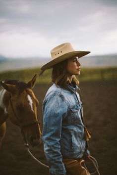 a woman wearing a cowboy hat standing next to a horse