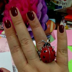 a ladybug ring sitting on top of a woman's hand with red nails